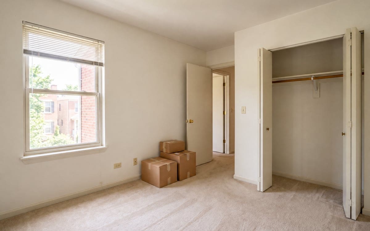 An empty carpeted bedroom on a move-out cleaning checklist, closet doors open and three moving boxes by the door.